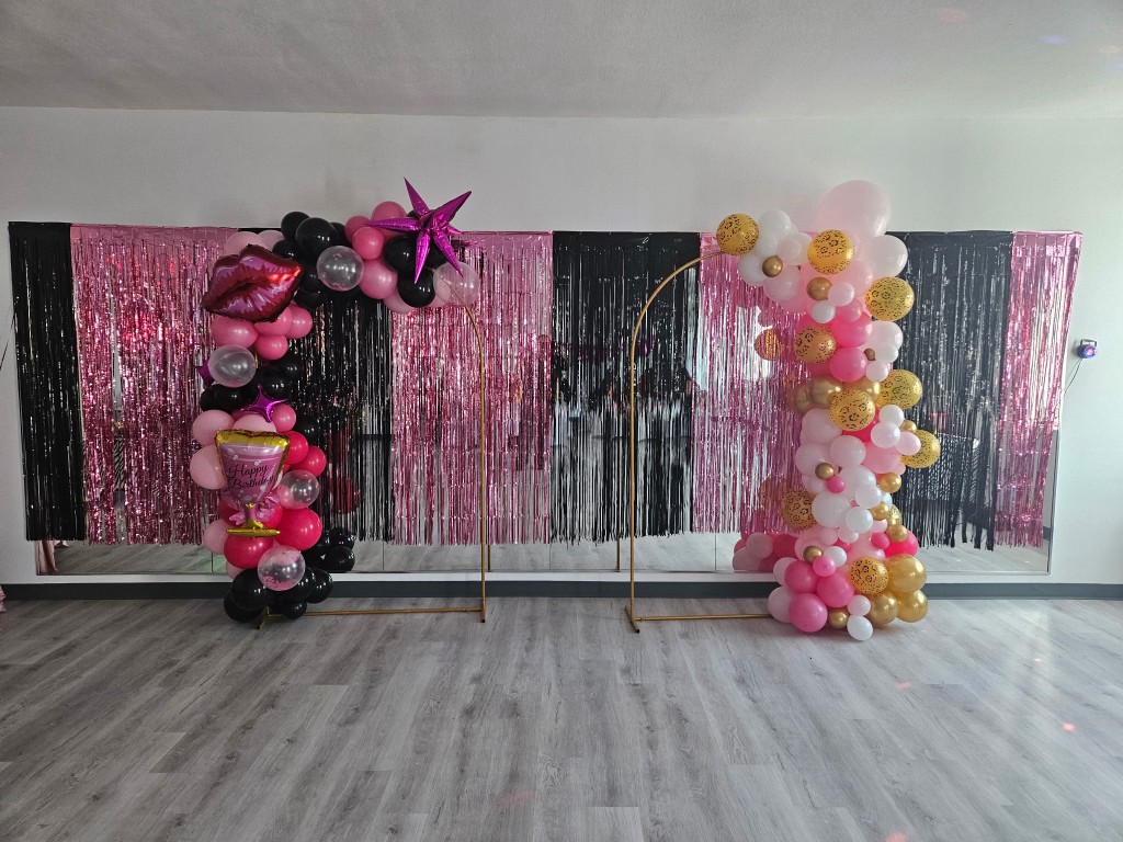 Studio party setup with gold balloon arches and pink and black fringe backdrop